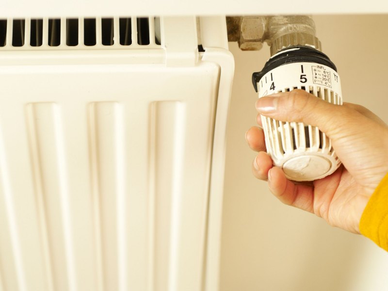 Hand turning a radiator thermostat valve to control home heating